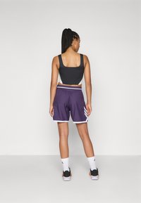 Top corto atletico nero e grigio abbinato a pantaloni corti viola con bordo bianco e tre strisce sui lati. Calzini bianchi e sneakers nere.