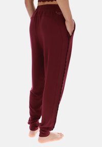 Pantaloni sportivi bordeaux con vestibilità comoda, vita elasticizzata, tasche laterali e dettaglio smerlato lungo la cucitura esterna. Tessuto elasticizzato.