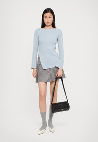Light blue ribbed sweater with flared cuffs, patterned mini skirt, gray knee-high socks, and a black crossbody bag. White pointed-toe shoes.