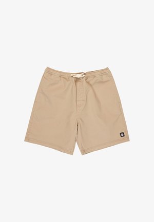 Chłopiec stoi z rękami w kieszeniach, ubrany w granatowy t-shirt, beżowe szorty, czarne skarpetki i granatowe trampki na białym tle.