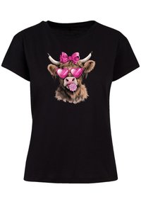 Black t-shirt featuring a graphic of a cow wearing pink heart-shaped sunglasses and a pink bow, holding a lollipop in its mouth.