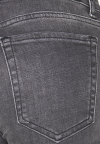 Jeans de mezclilla negra con diseño clásico de bolsillo trasero con costuras visibles, textura ligera y áreas sutilmente descoloridas.