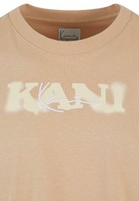 Beige cotton t-shirt with a round neckline and short sleeves, featuring a stylized "KANI" logo in a faded cream color and white embroidery.