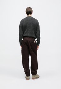 Conjunto informal que incluye un suéter acanalado gris oscuro y pantalones marrones de corte holgado con un parche de logo, combinados con botas marrón claro.