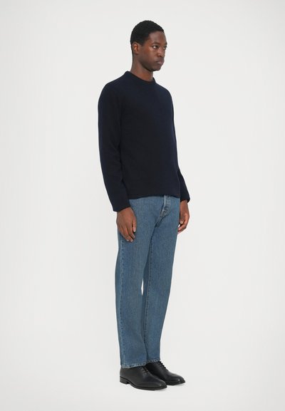 Marine crewneck trui, denim blauwe jeans en zwarte veterschoenen. Gladde textuur, klassieke pasvorm en rechtmodel ontwerp met minimale accenten.