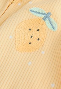 Oranžinė iškilusių juostų medžiaga su siuvinėtomis persikų spalvos gėlėmis ir žaliomis lapelėmis, pabrėžta mažais baltais taškeliais.