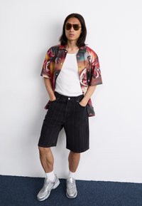 Korte mouw, multicolore overhemd met abstracte patronen, gecombineerd met donkere streepjesshorts en zilveren sportief schoenen.