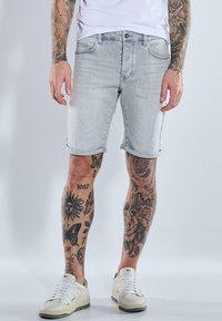 Light gray denim shorts with rolled hems, five pockets, and a button closure, worn with white sneakers. Decorated tattoos on visible legs.