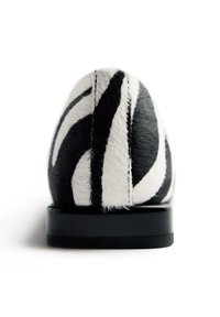 Zapato de estampado de cebra con un material texturizado similar al pelo en blanco y negro. Presenta una forma redondeada y una suela plana negra.
