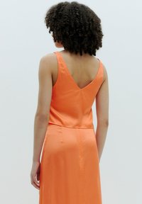 Oranje satijnen jurk met een V-rug en dunne bandjes, met een gladde textuur en een getailleerde taille, die tot halverwege de kuit reikt.