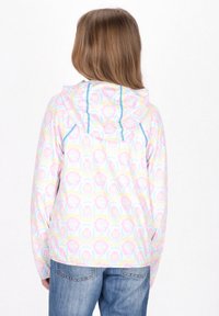 Giacca a fantasia colorata con design rosa, giallo e blu. Il cappuccio ha cuciture blu a contrasto. Indossata con jeans blu.
