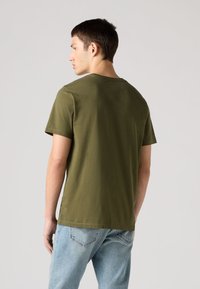 Olivno zelena bombažna majica s kratkimi rokavi, okroglim izrezom in sproščenim krojem, kombinirana s svetlo modrimi kavbojkami iz jeansa.