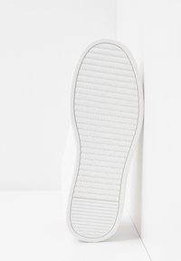 Vit sula på sneakers med texturerad gummiyta och horisontella samt vertikala räfflor för grepp; ren, minimalistisk design.