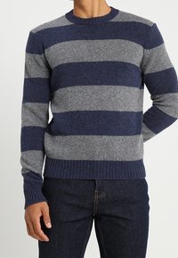 Mörkblå och grå randig ulltröja med rund halsringning, ribbstickade muddar och fåll. Mjuk textur med en normal passform.