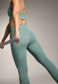 Set de antrenament verde mentă, care include un sutien sport cu bretele și colanți cu talie înaltă. Textură netedă cu o fit strâns, ținând o bandă de rezistență.