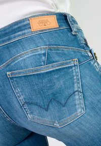 Jean en denim bleu avec une étiquette en cuir sur la ceinture et une couture distinctive des poches arrière en motif de vagues.