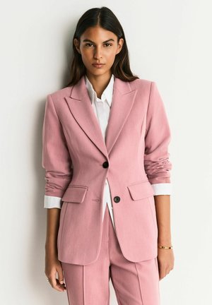 Light pink blazer with tailored fit, structured shoulders, single button closure, and two front pockets. White shirt and neutral background.