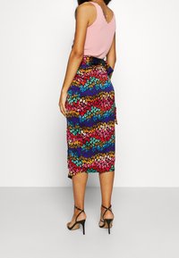 Jupe midi à motifs floraux dans des couleurs vives (bleu, rose, jaune, vert) avec un détail de taille nouée, associée à un haut sans manches rose.