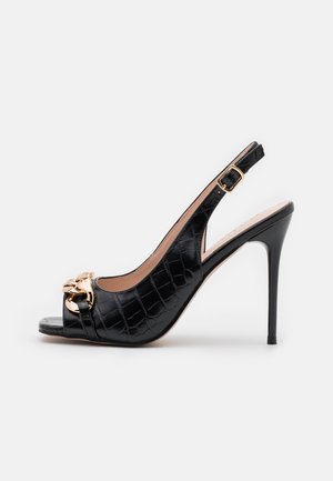 Sort højhælet slingback-sko med krokodillestribet tekstur og guldkædedetalje på den åbne tå, vist fra siden.