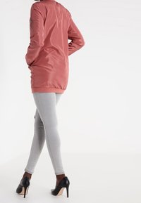 Light pink longer jacket with a stand collar, paired with light gray leggings and black high heels. Smooth texture and fitted design.