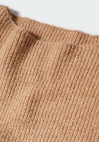 Beige ribattu kudos merasa weich. Jörnimne har vertikala slimar, som visar upp en mysig och varm material.