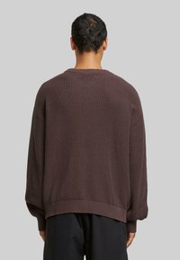 Brązowy sweter dziany z teksturowanym materiałem, z prążkowanymi mankietami i dołem. Dostępny w luźnym kroju z okrągłym dekoltem.