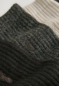 Drei gestrickte Kleidungsstücke in verschiedenen Grautönen und Beigefarben, die strukturierte Muster aufweisen und auf einem dezenten gestickten Logo.