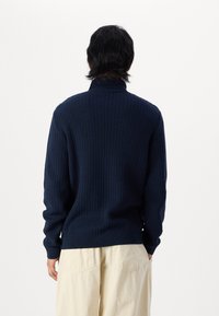 Suéter de color azul marino, de punto, con un cuello alto y dobladillo acanalado. Patrón texturizado y mangas largas, fabricado en una tela suave y flexible.