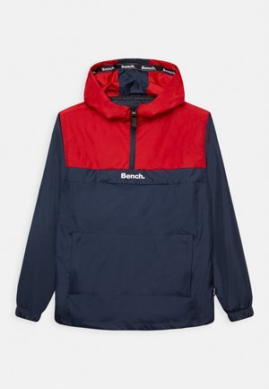 Coupe-vent rouge et marine avec un design à demi-zip, des poignets élastiques, une poche frontale et le logo "Bench." sur la poitrine. Texture légère et lisse.
