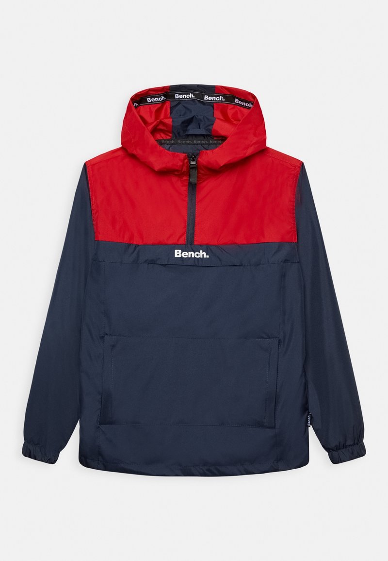 Coupe-vent rouge et marine avec un design à demi-zip, des poignets élastiques, une poche frontale et le logo "Bench." sur la poitrine. Texture légère et lisse.