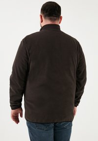 Sötétbarna bolyhos dzseki magas gallérral, hosszú ujjal és sima felülettel. Egyenes szabással rendelkezik, látható záródás nélkül.