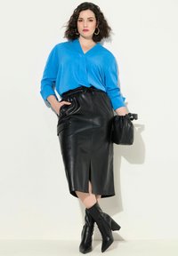 Blusa blu a maniche lunghe con scollo a V, abbinata a una gonna a tubino in pelle nera con spacco frontale e due tasche laterali. Stivali neri a punta.