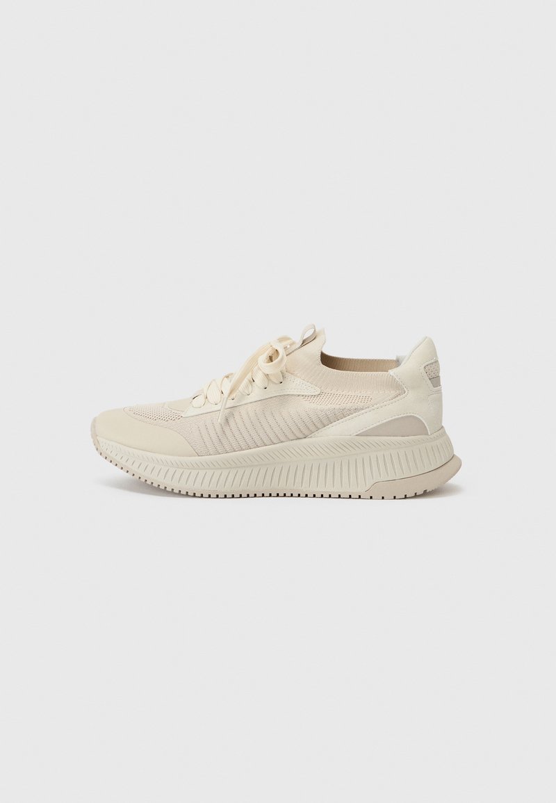 Beige athletic sneaker with a breathable mesh upper, lace closure, and a textured rubber sole for traction and cushioning.