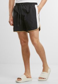 Svart-hvite svømshorts med snøring i livet, gullkant og sidelommer, laget av lett materiale.