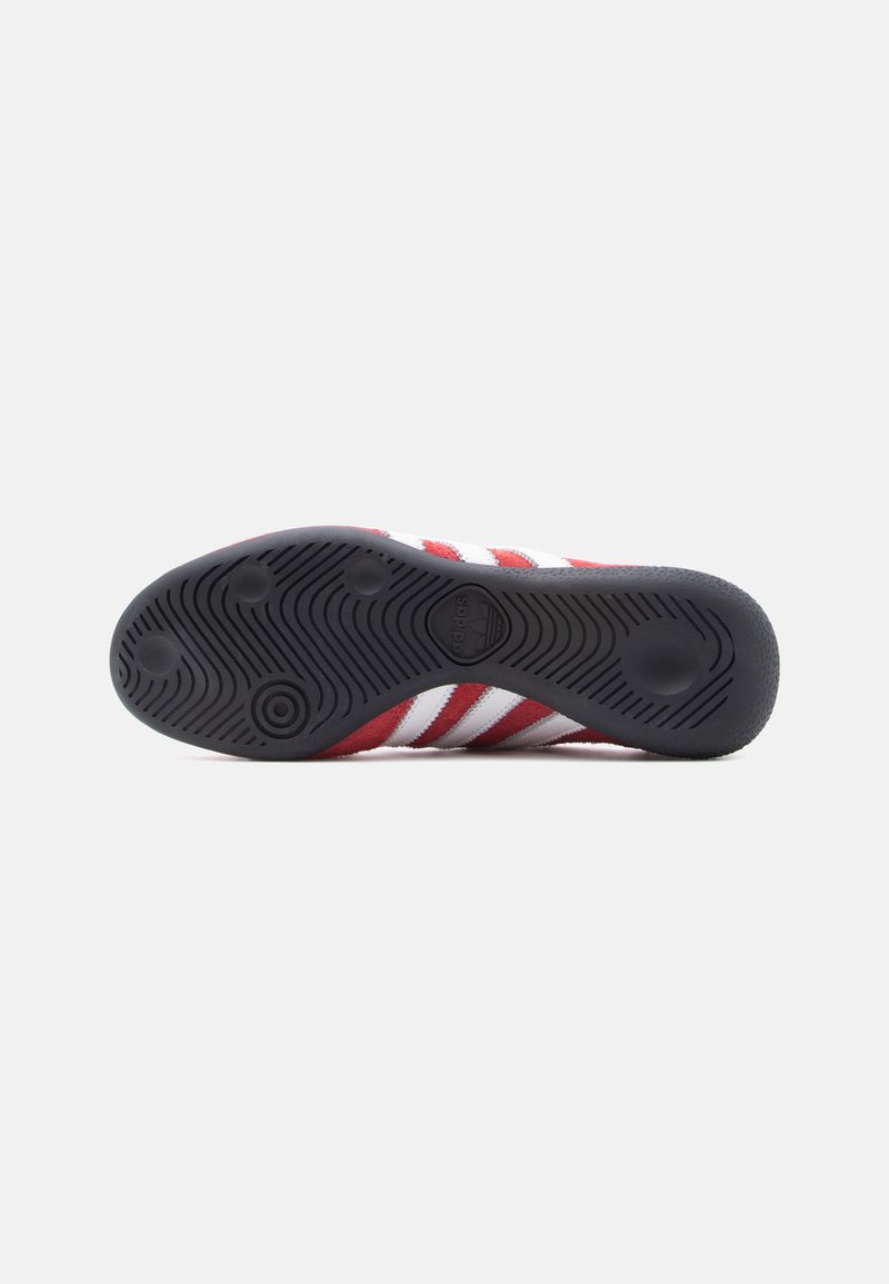 Red and white striped athletic shoe with a black rubber sole. Features textured grip pattern and prominent branding on the sole.
