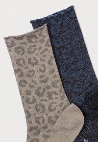 Dois pares de meias de leopardo brilhantes, uma em bege e cinza, a outra em preto e azul, dispostas em plano sobre uma superfície branca.