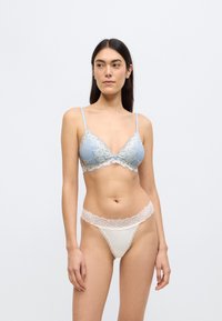 Μπλε ανοιχτό σουτιέν με δαντέλα και λουλουδάτες λεπτομέρειες, συνοδευόμενο από λευκό στρινγκ με δαντελένια ζώνη μέσης, και τα δύο με απαλή υφή.