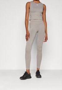 Béžový atletický crop top a legíny, s hladkou texturou, přiléhavým střihem a kontrastními švy. Černé tenisky dokončují outfit.