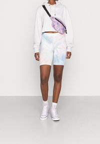 Haut à capuche court rose clair ; shorts de vélo tie-dye pastel en bleu, rose et blanc ; sac banane violet ; baskets montantes blanches avec des accents roses.