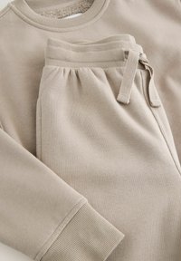Set aus beigem Sweatshirt und Hose aus weicher Baumwolle. Mit gerippten Manschetten, einem Kordelzugbund und glatter Textur.