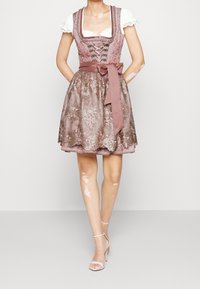 La robe présente un corsage ajusté avec un laçage à l'avant, des manches courtes bouffantes et une jupe longueur genou en dentelle florale rose et marron avec une ceinture ruban.