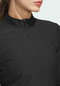 Zwarte gestructureerde langslurf top met hoge kraag en een halve rits, met een gladde textuur en naaddetails op de schouders.