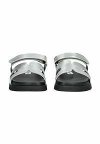 Sandali argentati con due cinturini regolabili, dettagli intagliati e suola nera. Design piatto adatto per un abbigliamento casual.