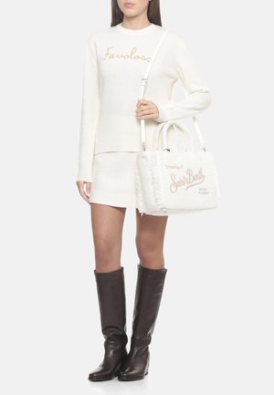 Maglione bianco lavorato a maglia con la scritta "Favoloso" in oro, abbinato a una minigonna bianca testurizzata e una borsa pelosa bianca con scritta rosa. Stivali marroni al ginocchio.