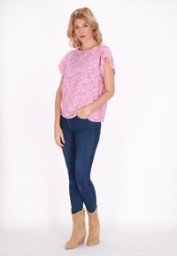 En blus med rosa paisleymönster och korta fladderärmar, tillsammans med slim fit blå jeans och ljusbruna ankelstövlar.