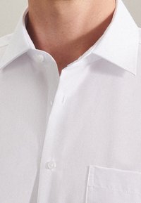 Bílá košile na knoflíky s klasickým límcem, s náprsní kapsou a hladkou strukturovanou látkou. Jednoduchý design a střih na míru.