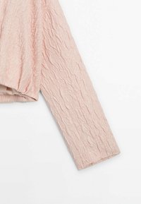 Veste rose clair à manches longues avec un tissu texturé froissé, présentée sur un fond blanc.
