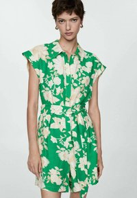 Groene bloemen jurkje met korte mouwen, kraag en tailleband. Bevat grote beige bloemenpatronen op een felgroene achtergrond.