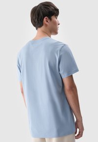 Jasnoniebieska koszulka z krótkim rękawem z bawełny, z okrągłym dekoltem i luźnym krojem, z gładkim tyłem i minimalnymi detalami.