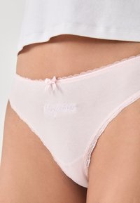 Ropa interior de algodón rosa en estilo bikini con detalles de encaje, que presenta un texto bordado "Confianza" en la parte frontal y un pequeño lazo en la parte trasera.